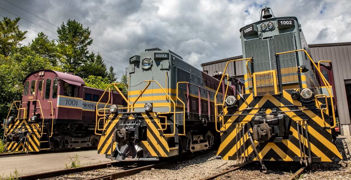 Three large trains side by side on a train track with a cloudy summer background