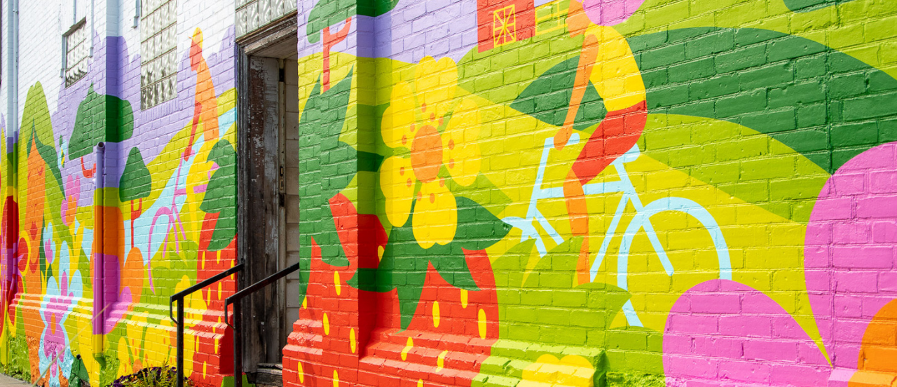 Vibrantly painted brick wall depicting a summer scene of bikers, fruit and flowers